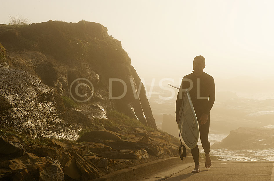 A male surfer walks up from the surf after an early morning surf, Norah