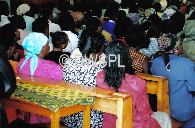 INTERIOR VIEW SHOWS COLOURFUL CLOTHING OF CONGREGATION DURING MASS IN CATHOLIC CHURCH IN NAIROBI